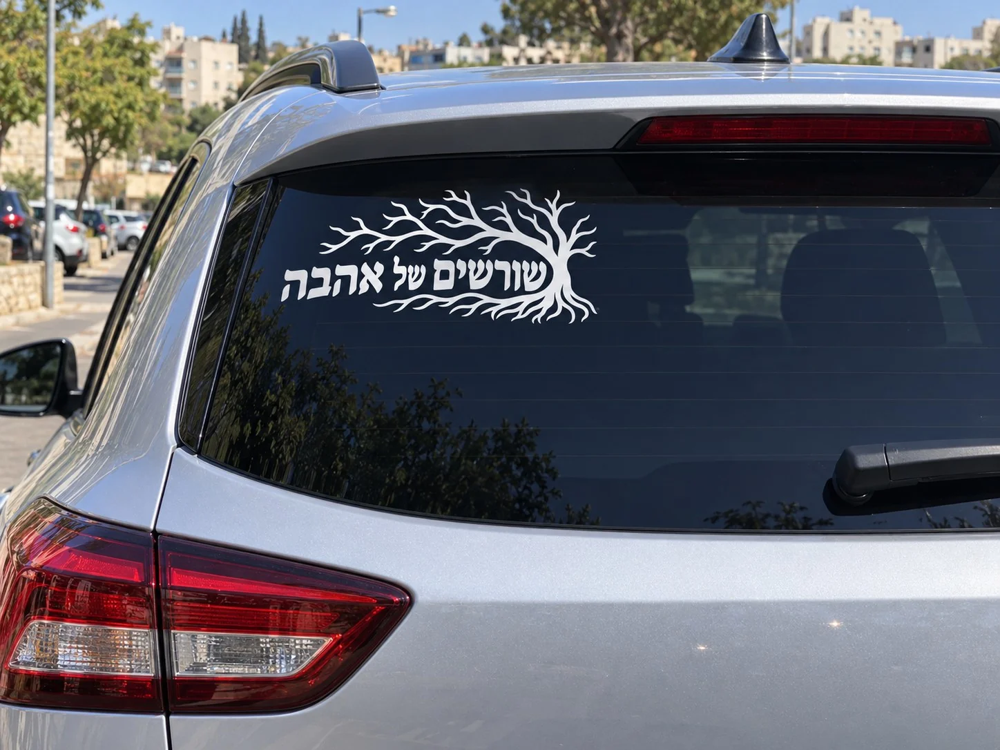 מדבקה שחורה עם כיתוב 'שורשים של אהבה' על השמשה האחורית של רכב חום ברחוב עירוני.