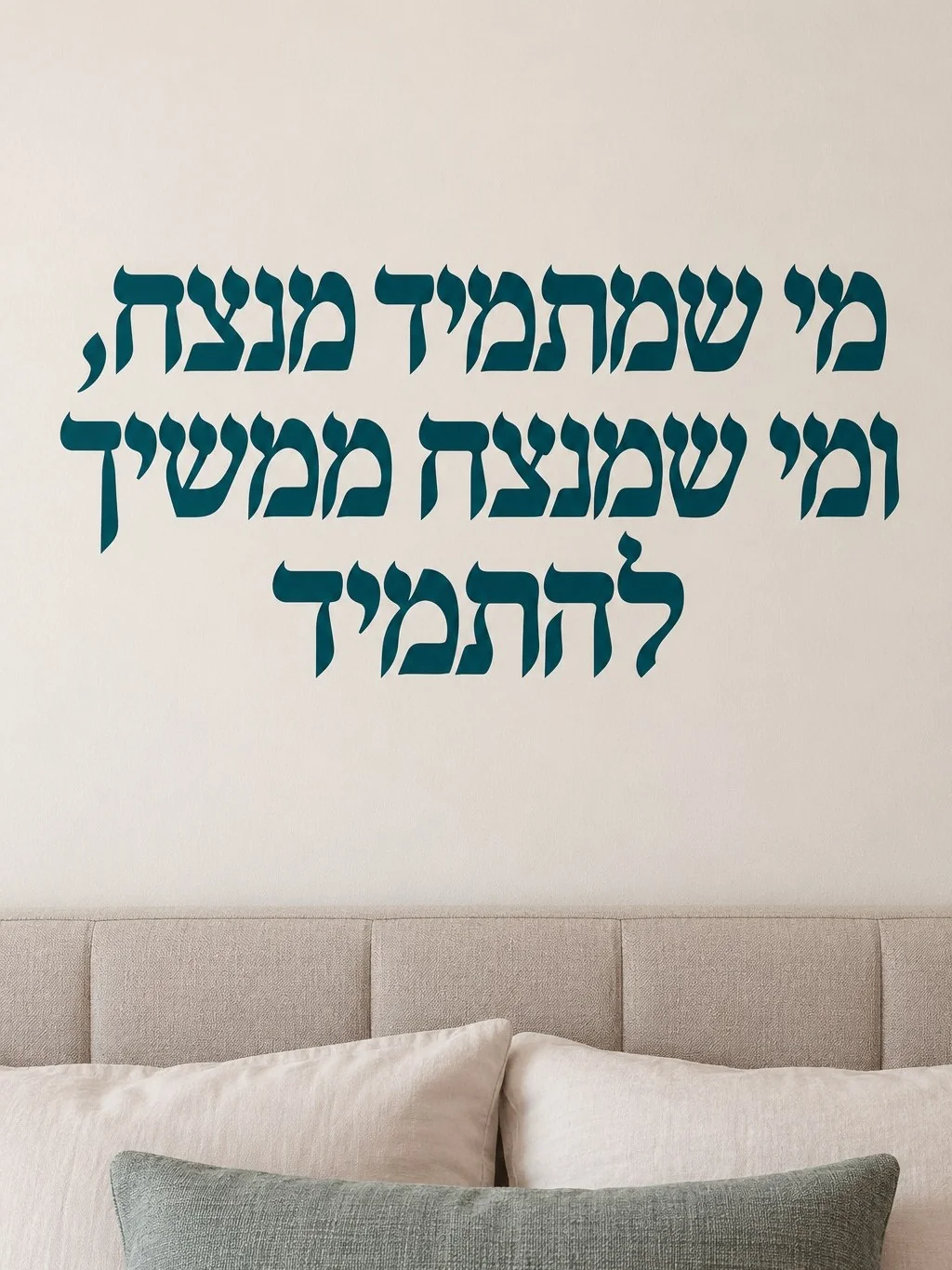 מדבקת טקסט עברי שחור על רקע לבן, על קיר בסלון עם ספה כהה ושולחן זכוכית